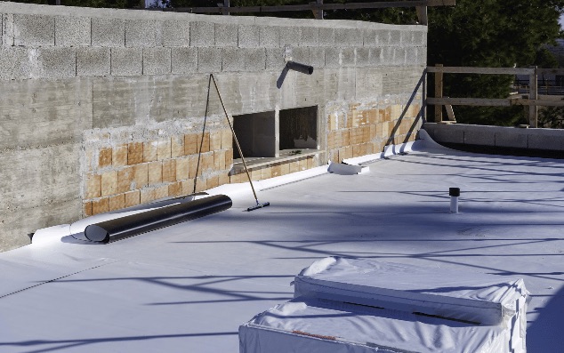 New flat roof membrane being laid against a stone wall