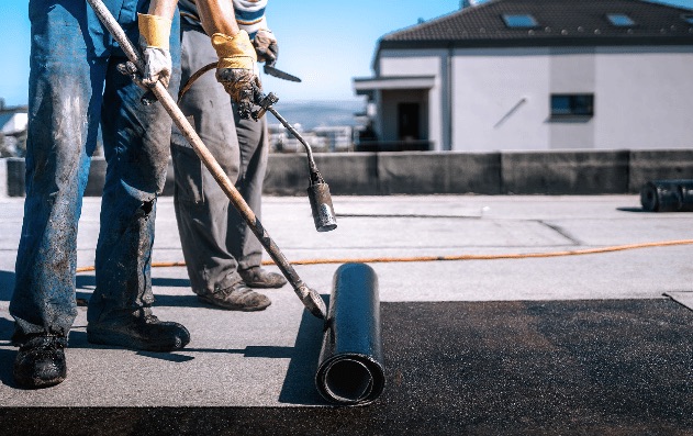 Roofers rolling out torch-on felt on a flat roof