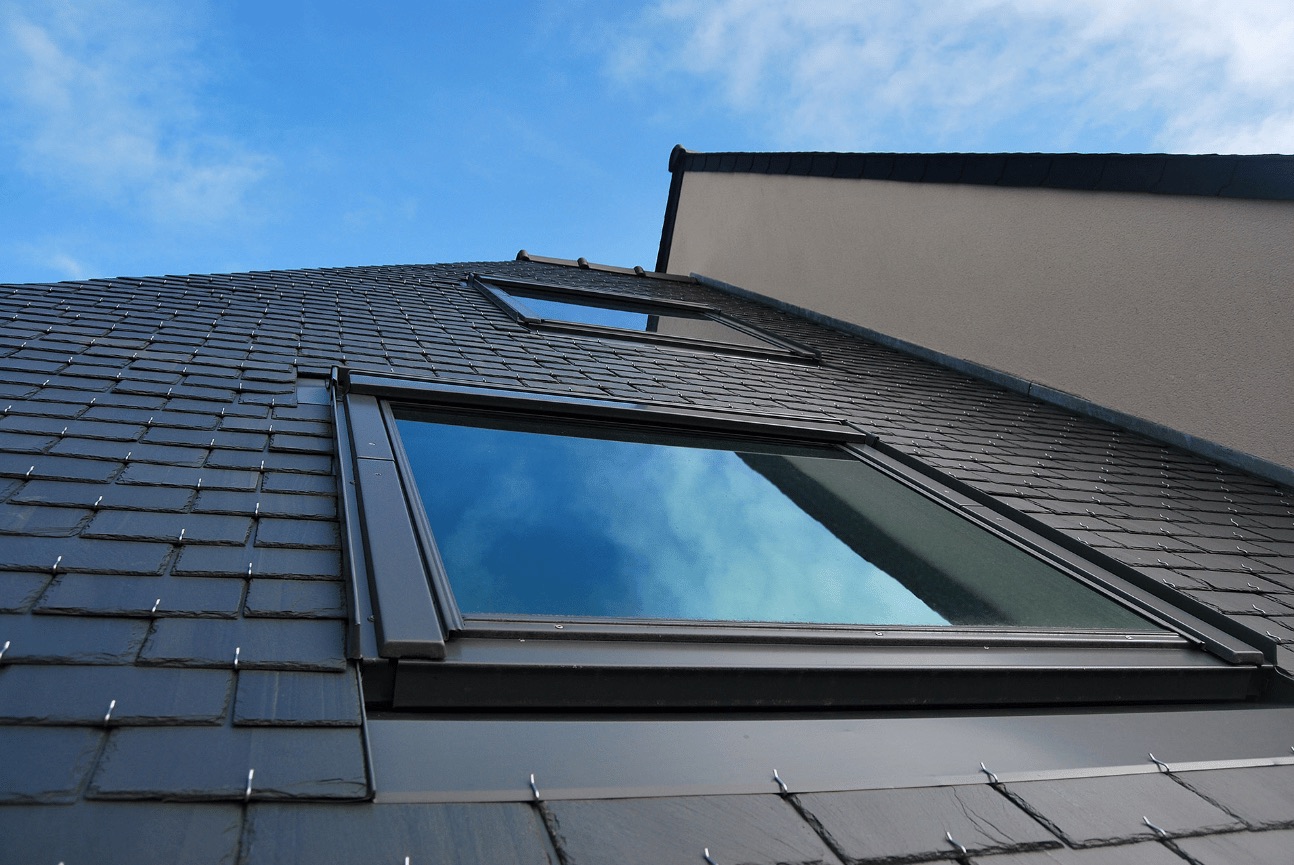 Slate roof with a flush roof window reflecting blue sky